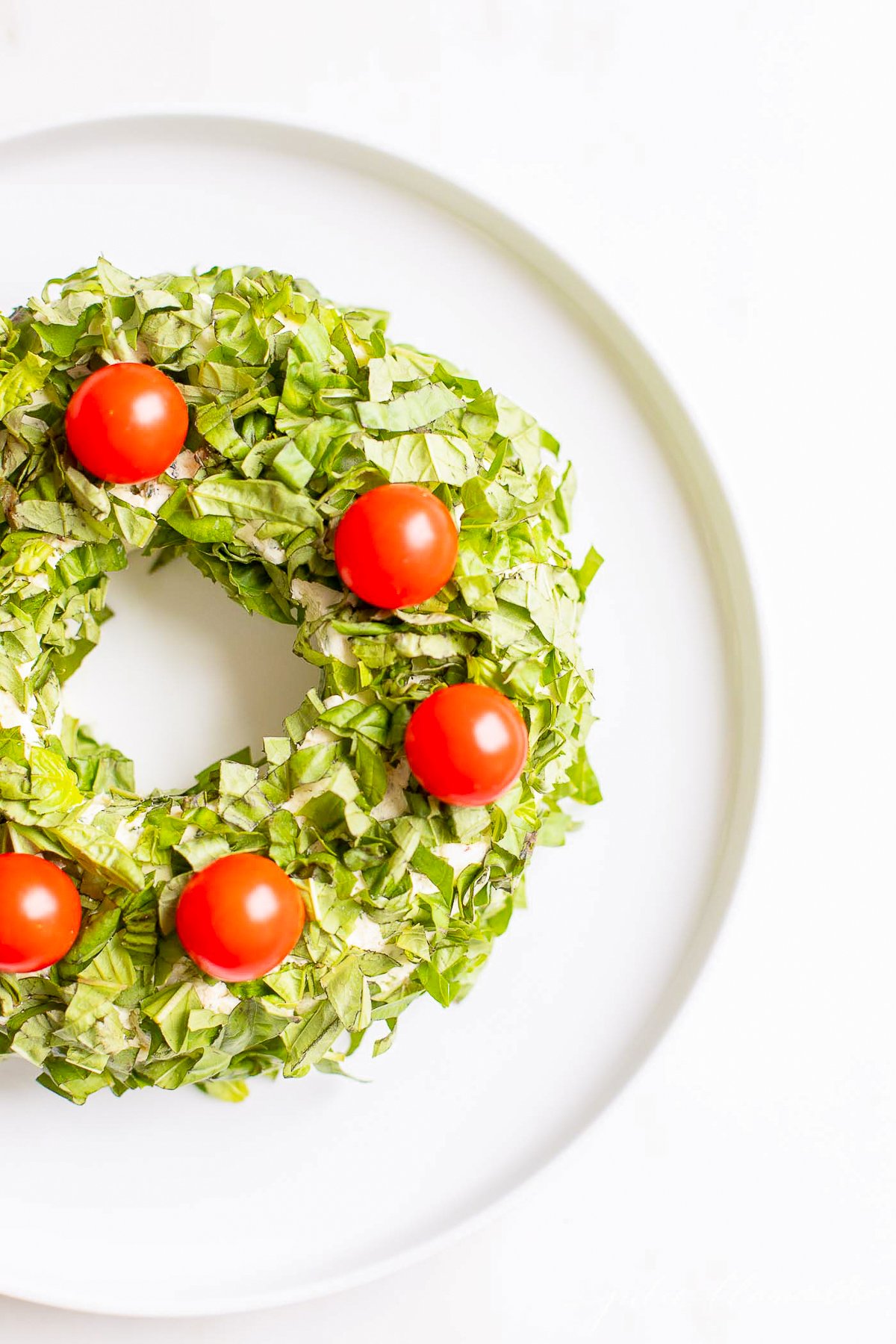 A pesto cheese ball topped with cherry tomatoes on a white plate.