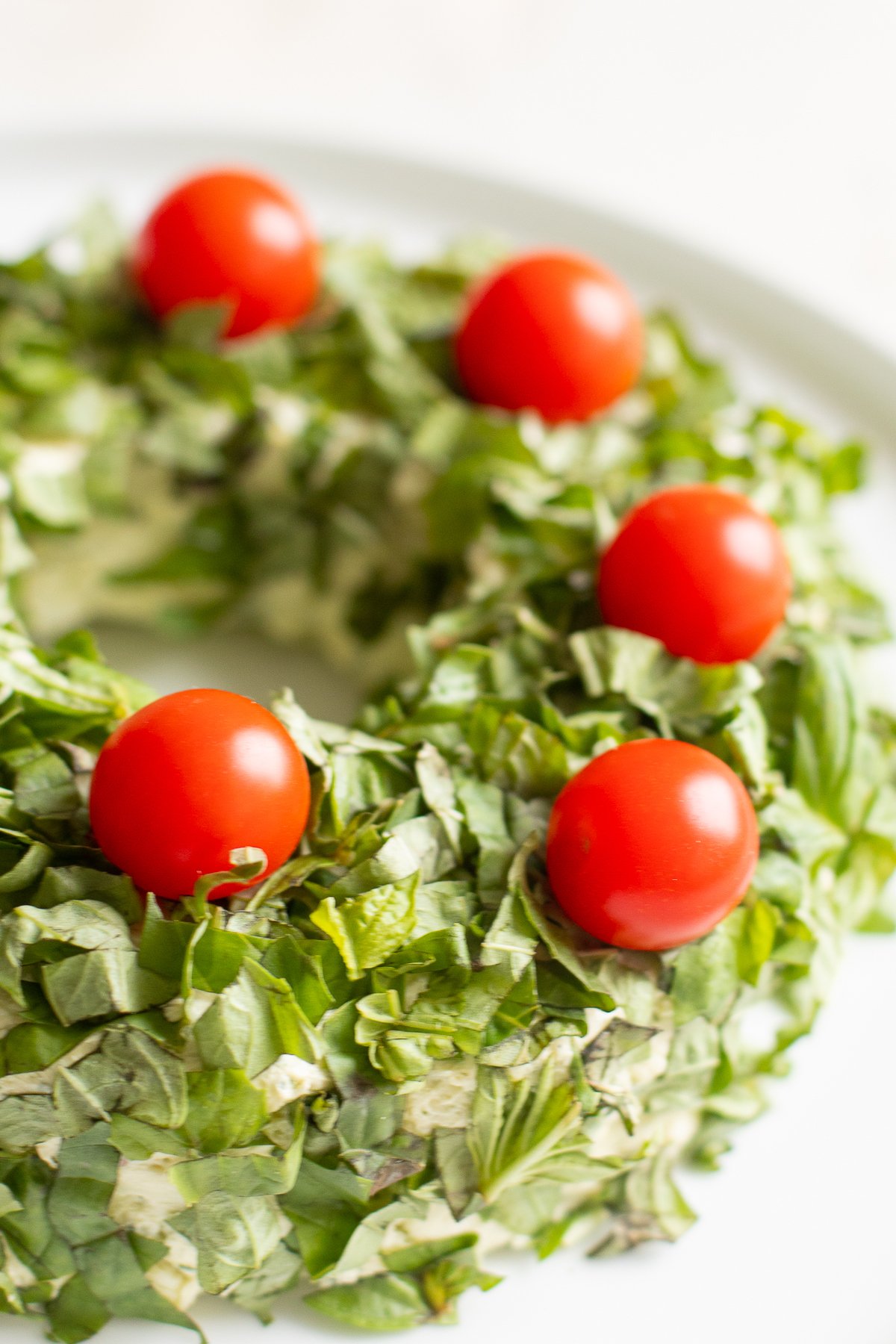 A pesto cheese ball topped with cherry tomatoes on a white plate.