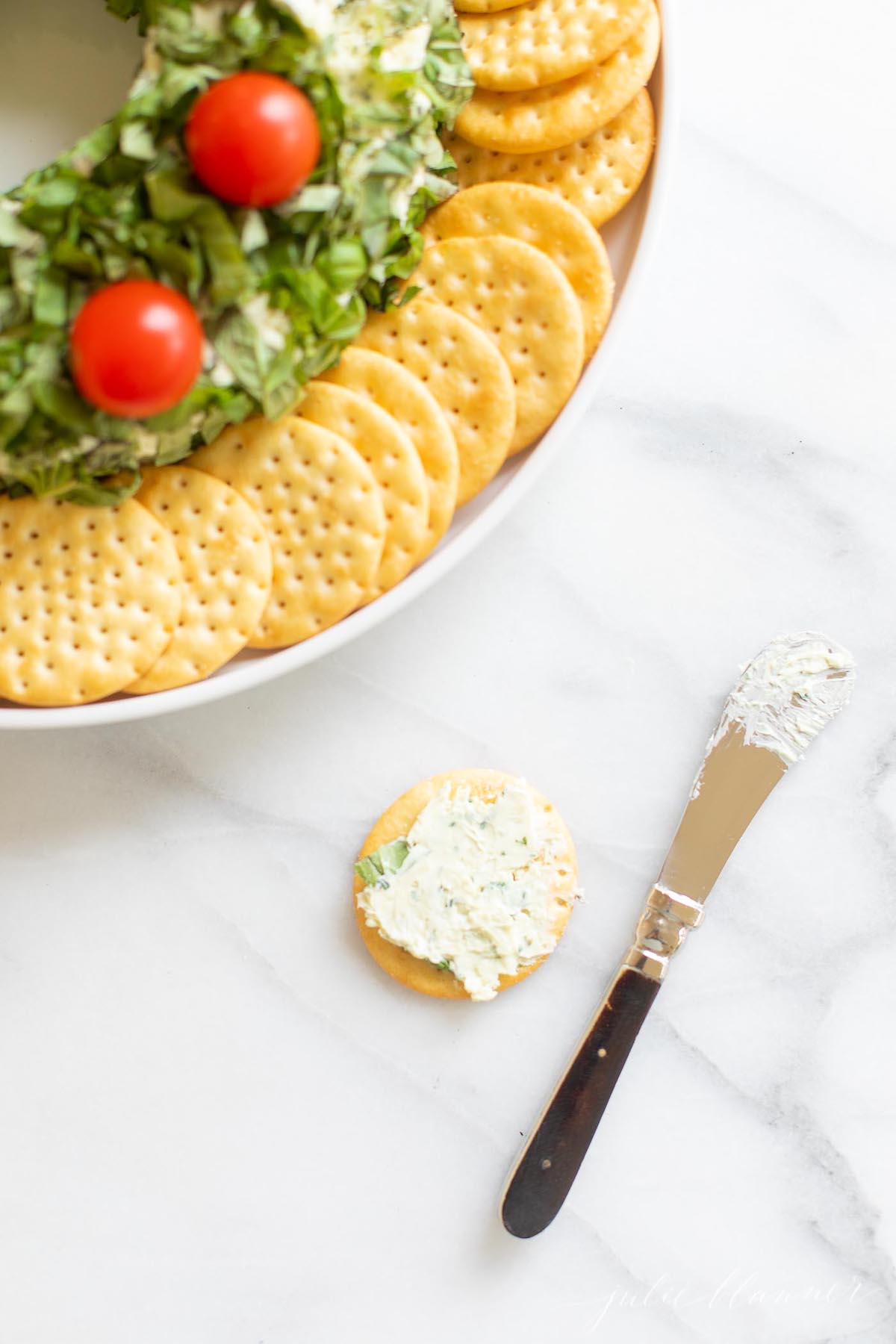 A pesto cheese ball topped with cherry tomatoes on a white plate.