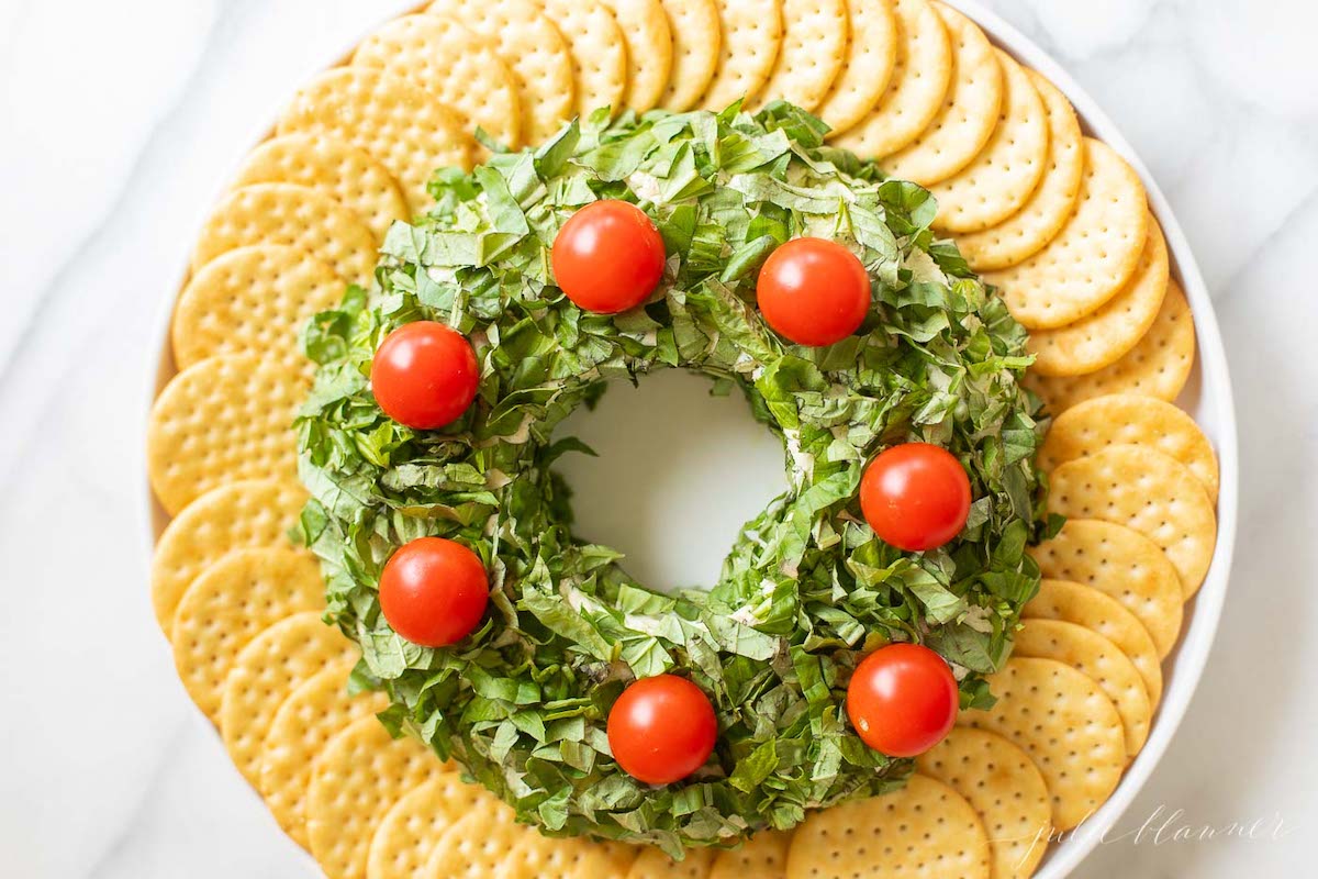 A pesto cheese ball topped with cherry tomatoes on a white plate.