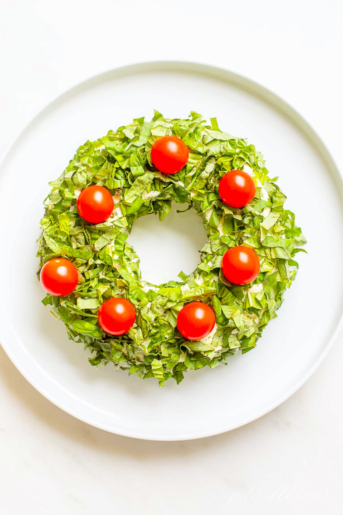 A pesto cheese ball topped with cherry tomatoes on a white plate.