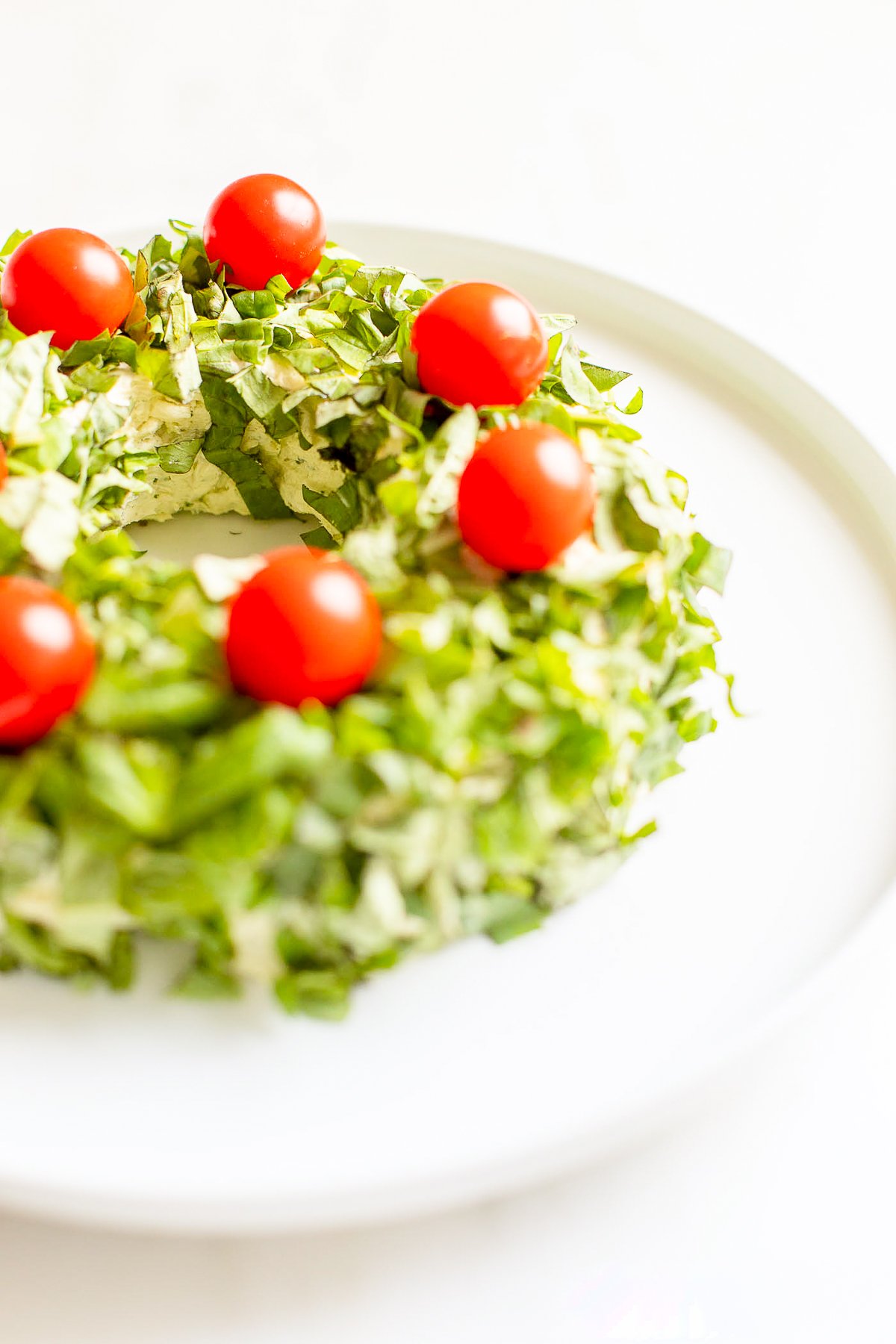 A pesto cheese ball topped with cherry tomatoes on a white plate.