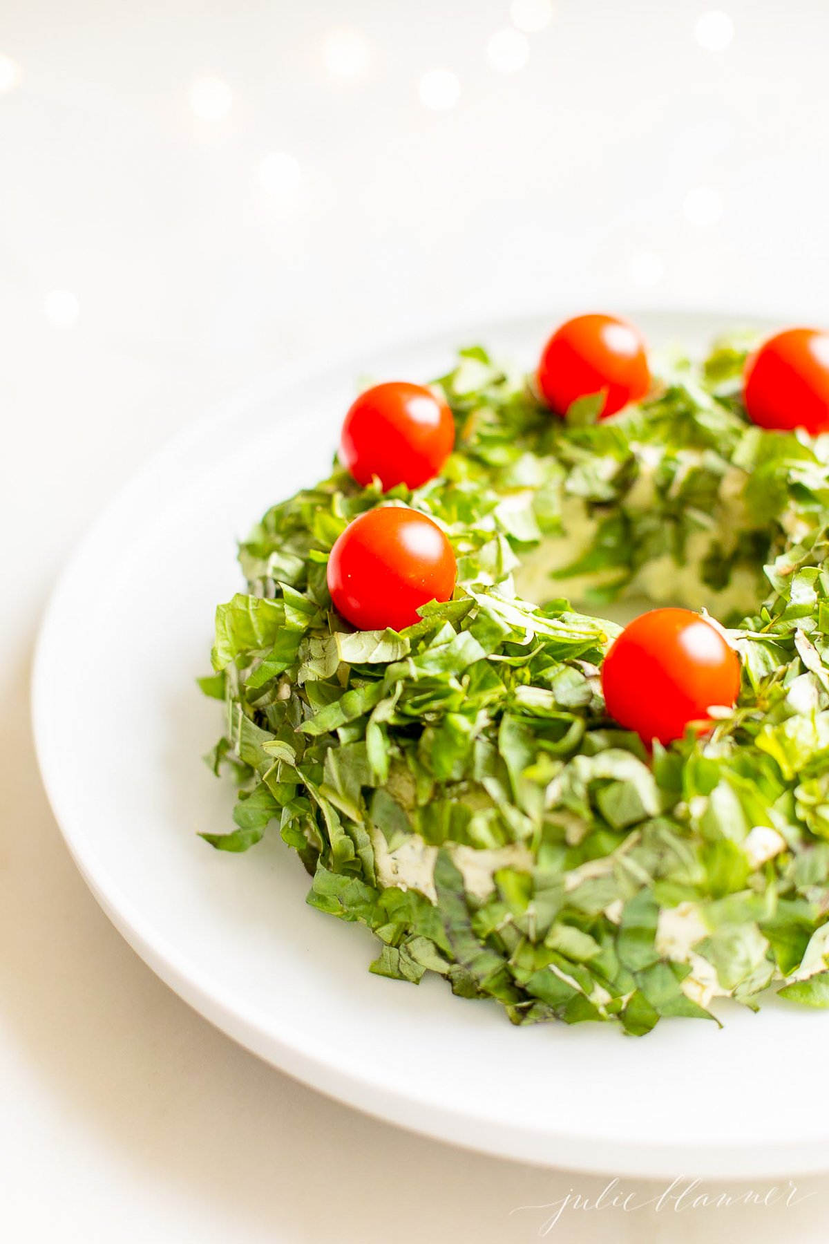 A pesto cheese ball topped with cherry tomatoes on a white plate.