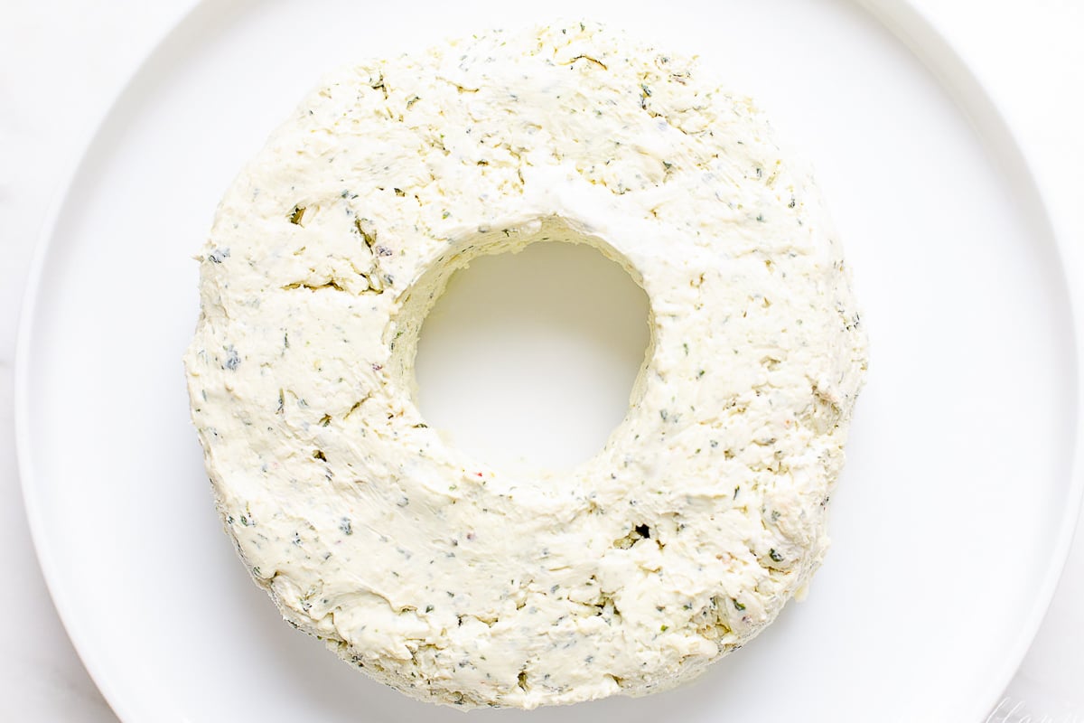 A pesto cheese ball on a white plate, before decorating