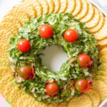 A plate with a wreath made of pesto cheese ball and tomatoes.