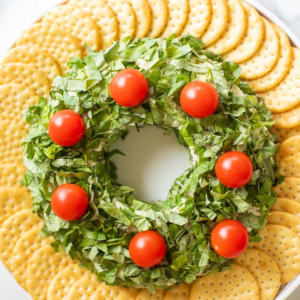 A plate with a wreath made of pesto cheese ball and tomatoes.