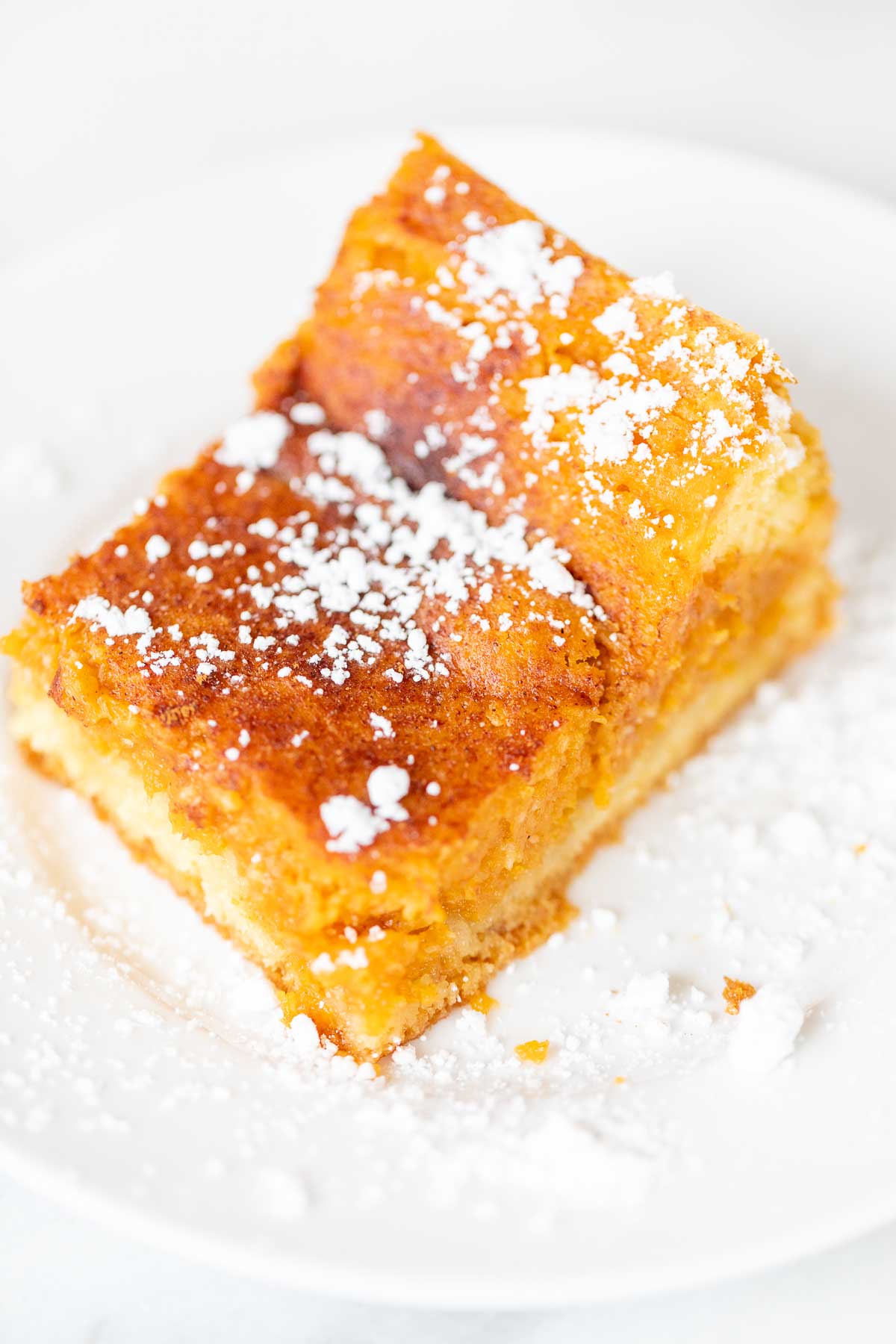 A slice of pumpkin gooey butter cake on a white plate, dusted with powdered sugar.