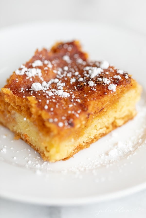 A slice of pumpkin gooey butter cake on a white plate, dusted with powdered sugar.