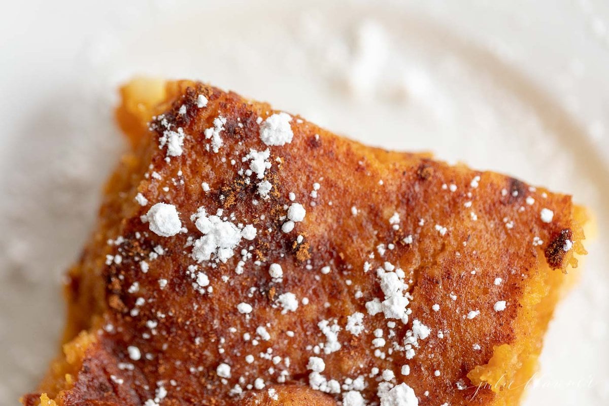 A slice of pumpkin gooey butter cake on a white plate, dusted with powdered sugar.