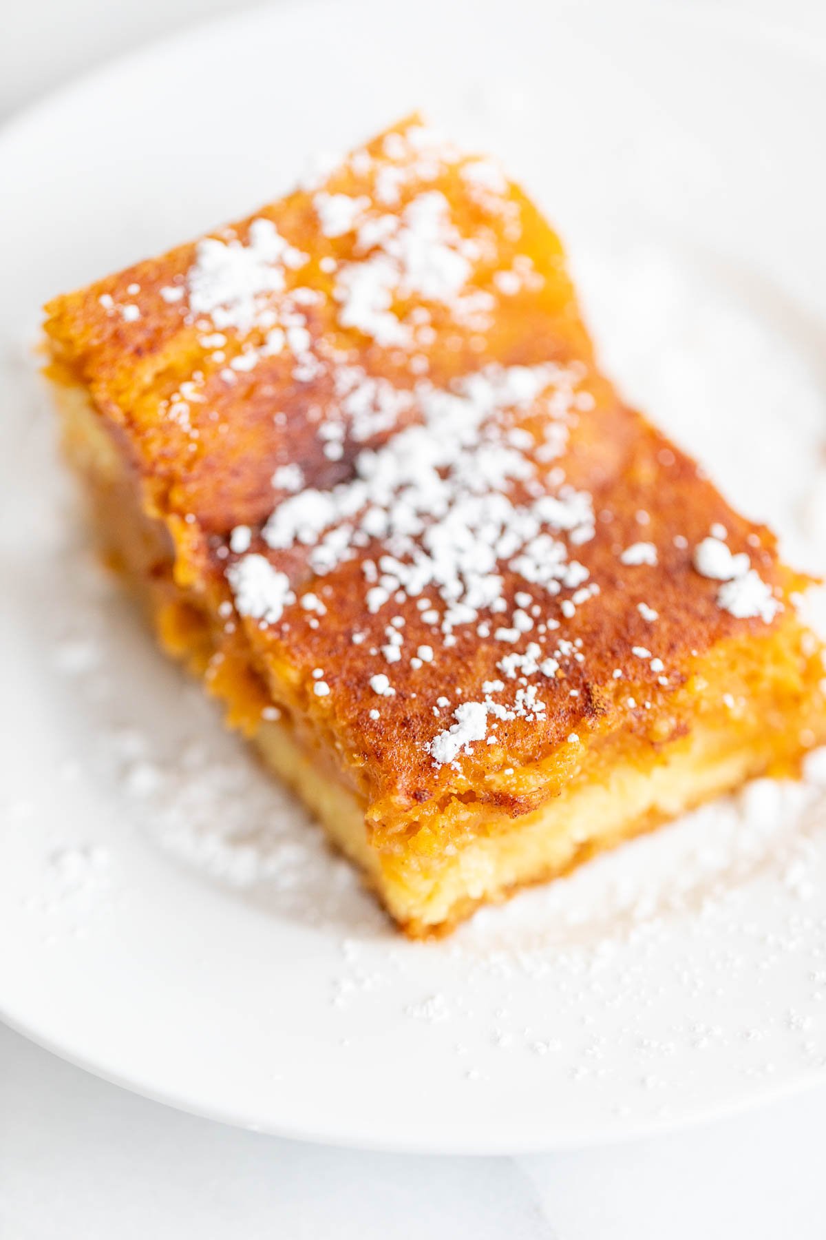 A slice of pumpkin gooey butter cake on a white plate, dusted with powdered sugar.