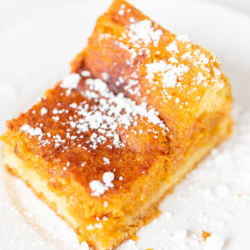 A slice of pumpkin gooey butter cake on a white plate, dusted with powdered sugar.