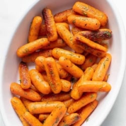 A white cast iron baking pan filled with roasted baby carrots