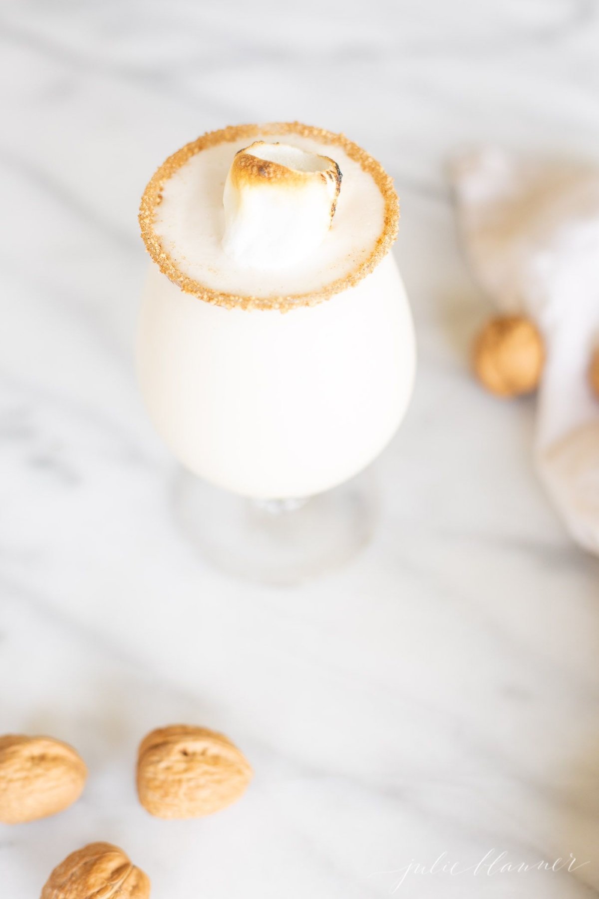 An ice cream and amaretto snowball cocktail in a stemmed glass, garnished with a toasted marshmallow, on a marble countertop.