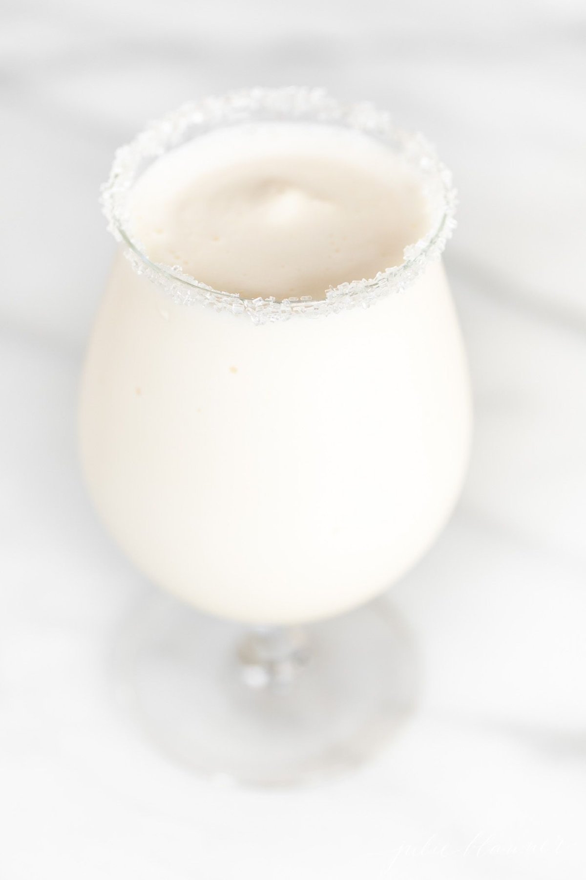 An ice cream and amaretto snowball cocktail in a stemmed glass, on a marble countertop. 