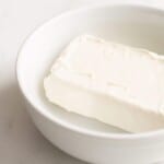 White bowl with a block of cream cheese inside.