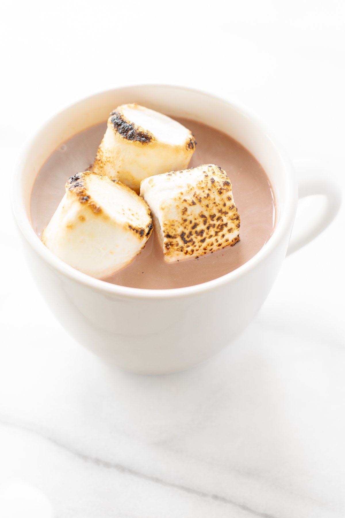 A white mug full of boozy hot chocolate, topped with toasted marshmallows.