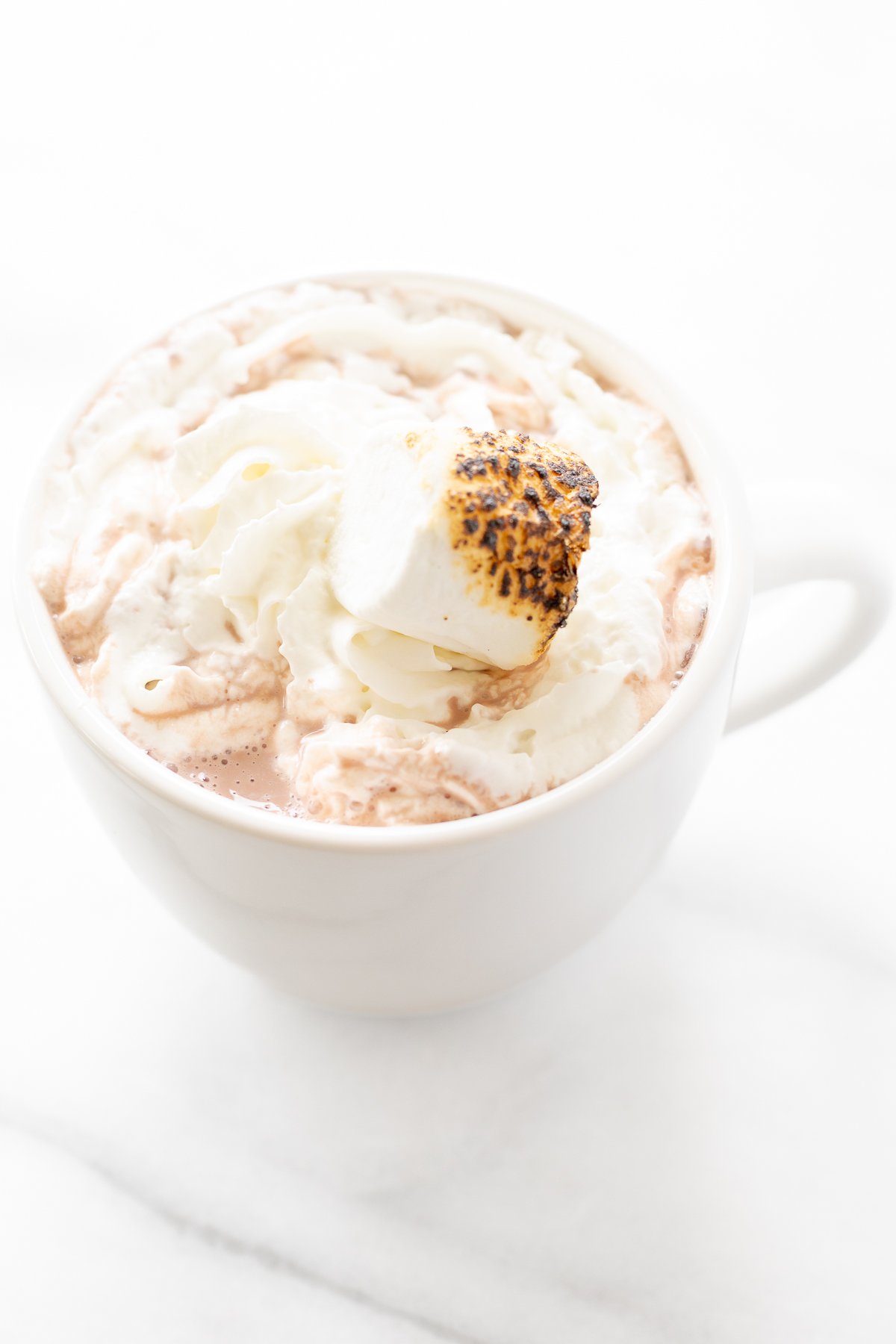 A white mug full of boozy hot chocolate, topped with whipped cream and toasted marshmallows.