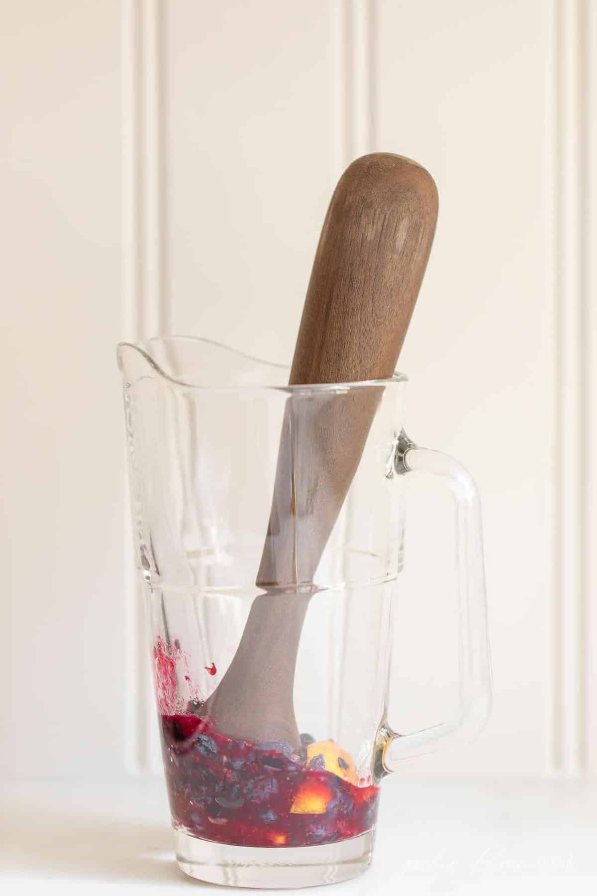 Clear pitcher, white surface, muddler inside smashing fruit for a bourbon smash recipe.