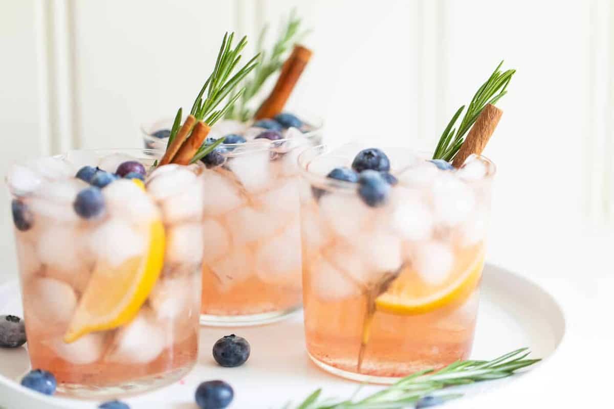 Trio of clear glasses full of a whiskey smash recipe with rosemary and cinnamon stick for garnish.