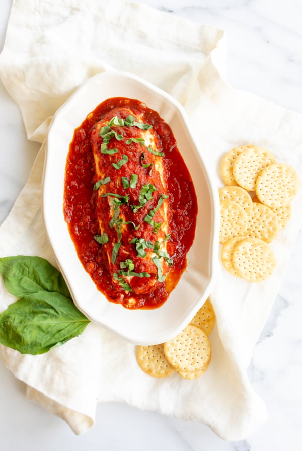 A white plate with a meatball covered in sauce and crackers, topped with queso de cabra con tomate.