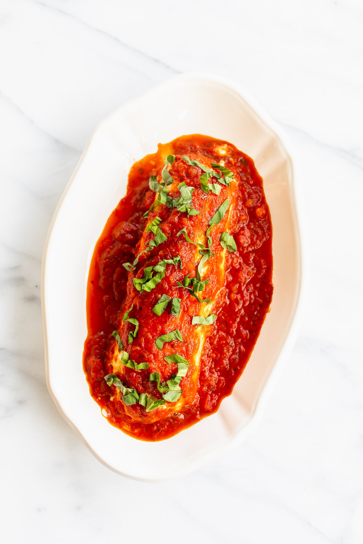 A plate with a stuffed eggplant topped with queso de cabra and tomato sauce.