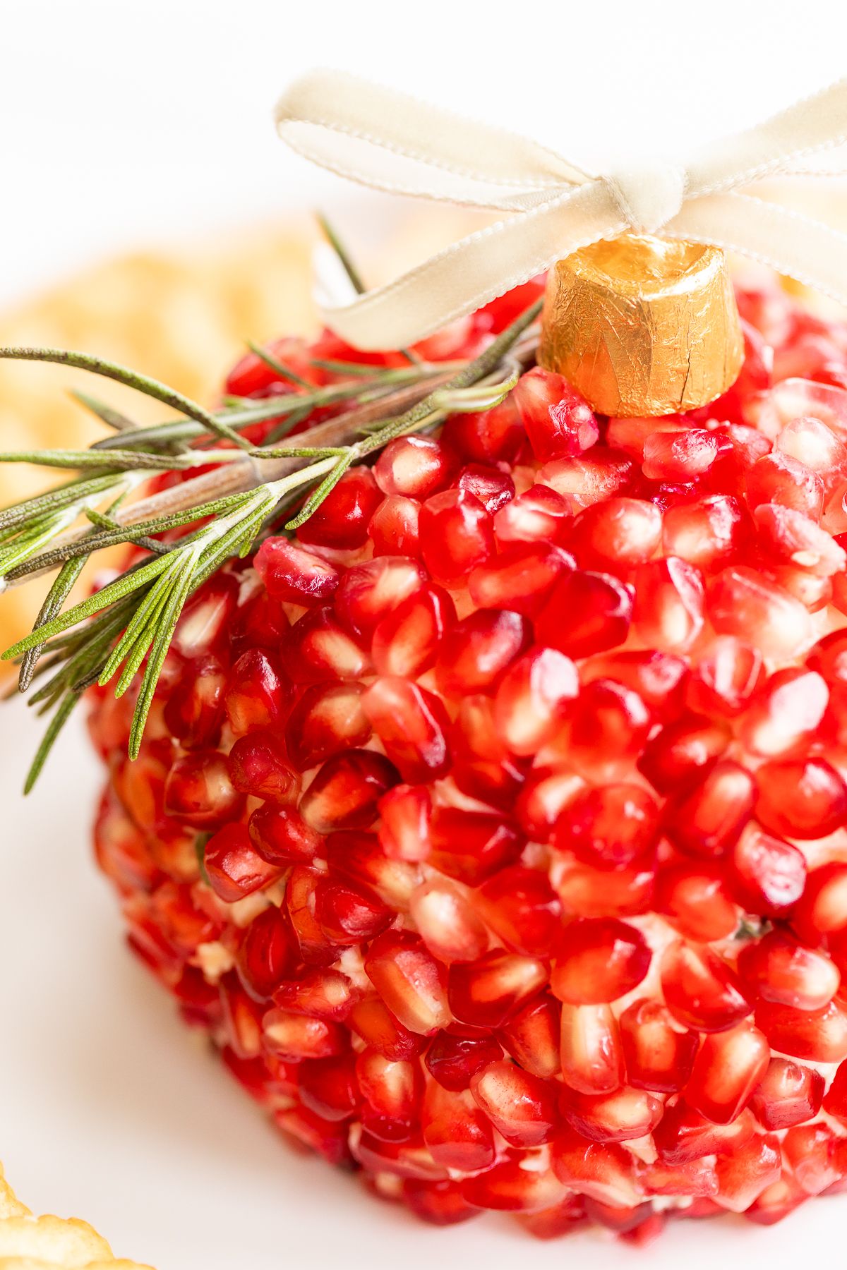 A pomegranate Christmas cheese ball shaped into an ornament, surrounded by crackers on a round white plate.