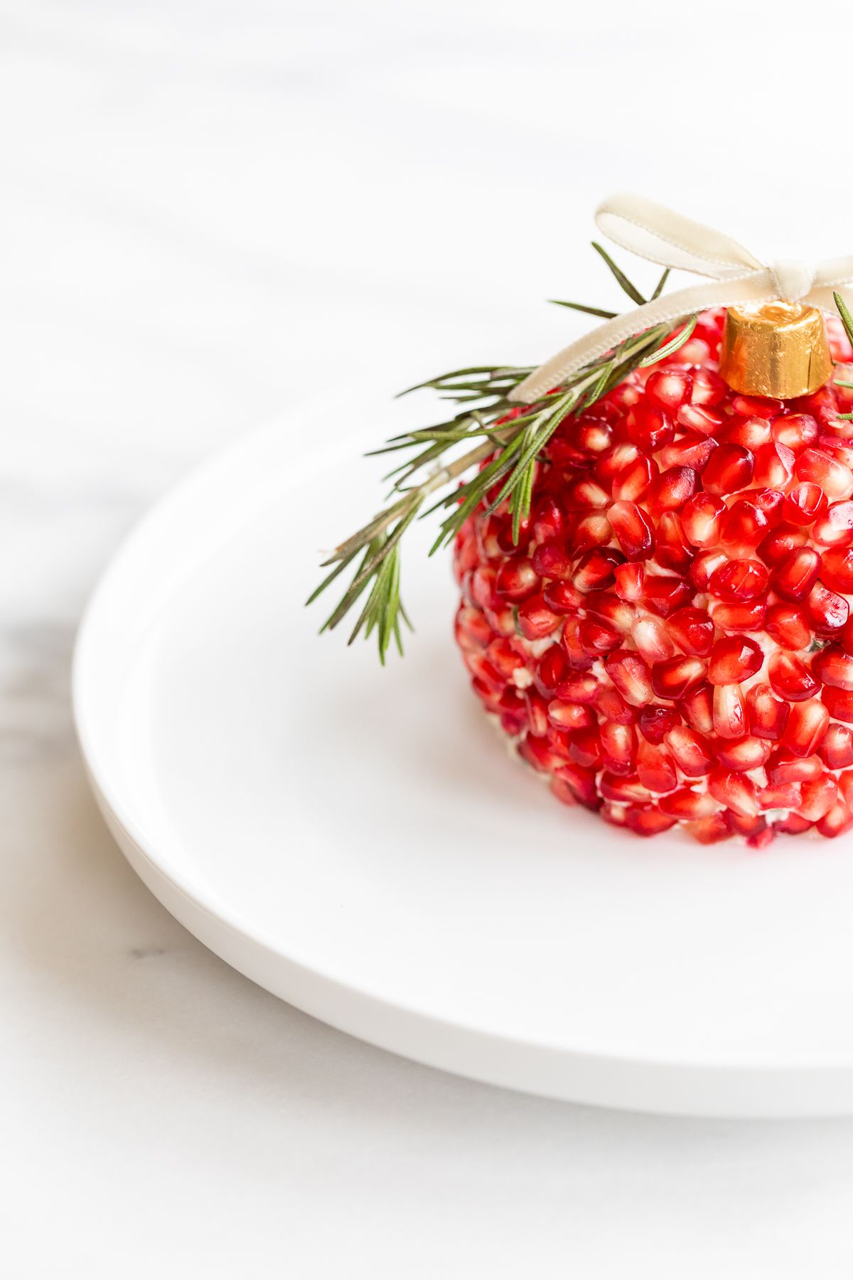 A pomegranate Christmas cheese ball shaped into an ornament on a round white plate.