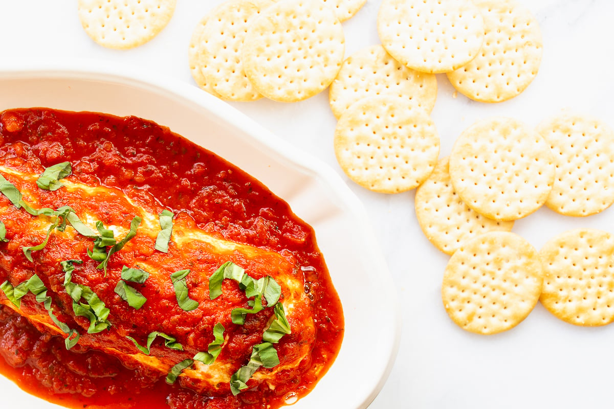 A white dish with a piece of fish covered in sauce and queso de cabra.