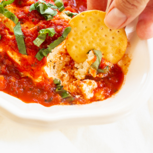 A person is dipping a cracker into a dish of queso de cabra.