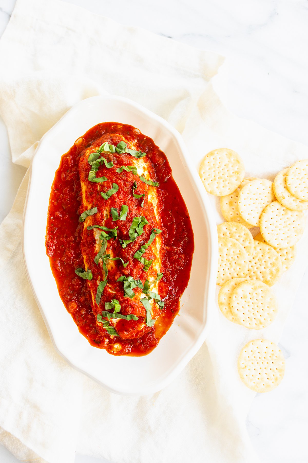 A plate of queso de cabra con tomate with a meatball covered in sauce and crackers.