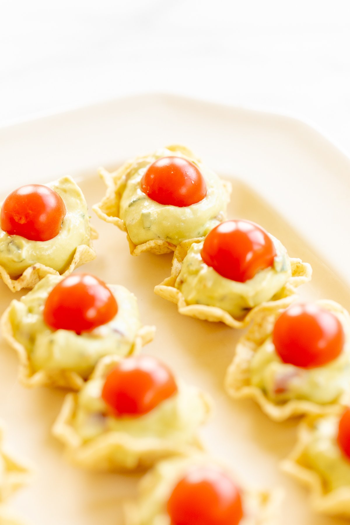 A white tray full of guacamole bites made from tortilla chips, topped with sliced cherry tomatoes.