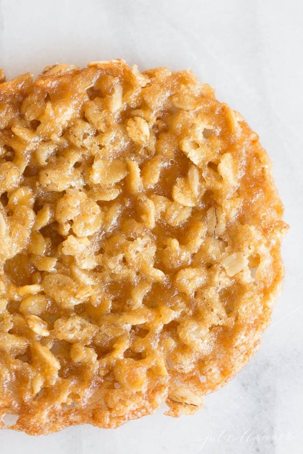 A single oatmeal lace cookie place on a marble countertop