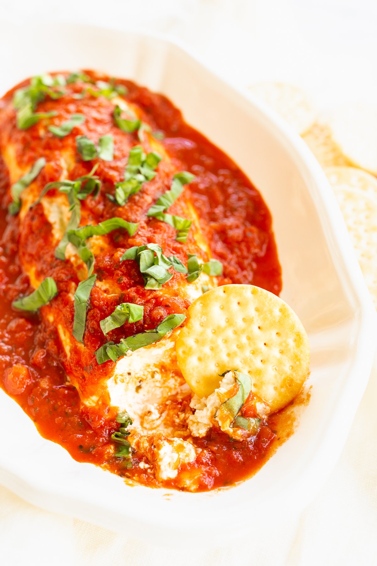 A white plate with a pizza covered in sauce and goat cheese.