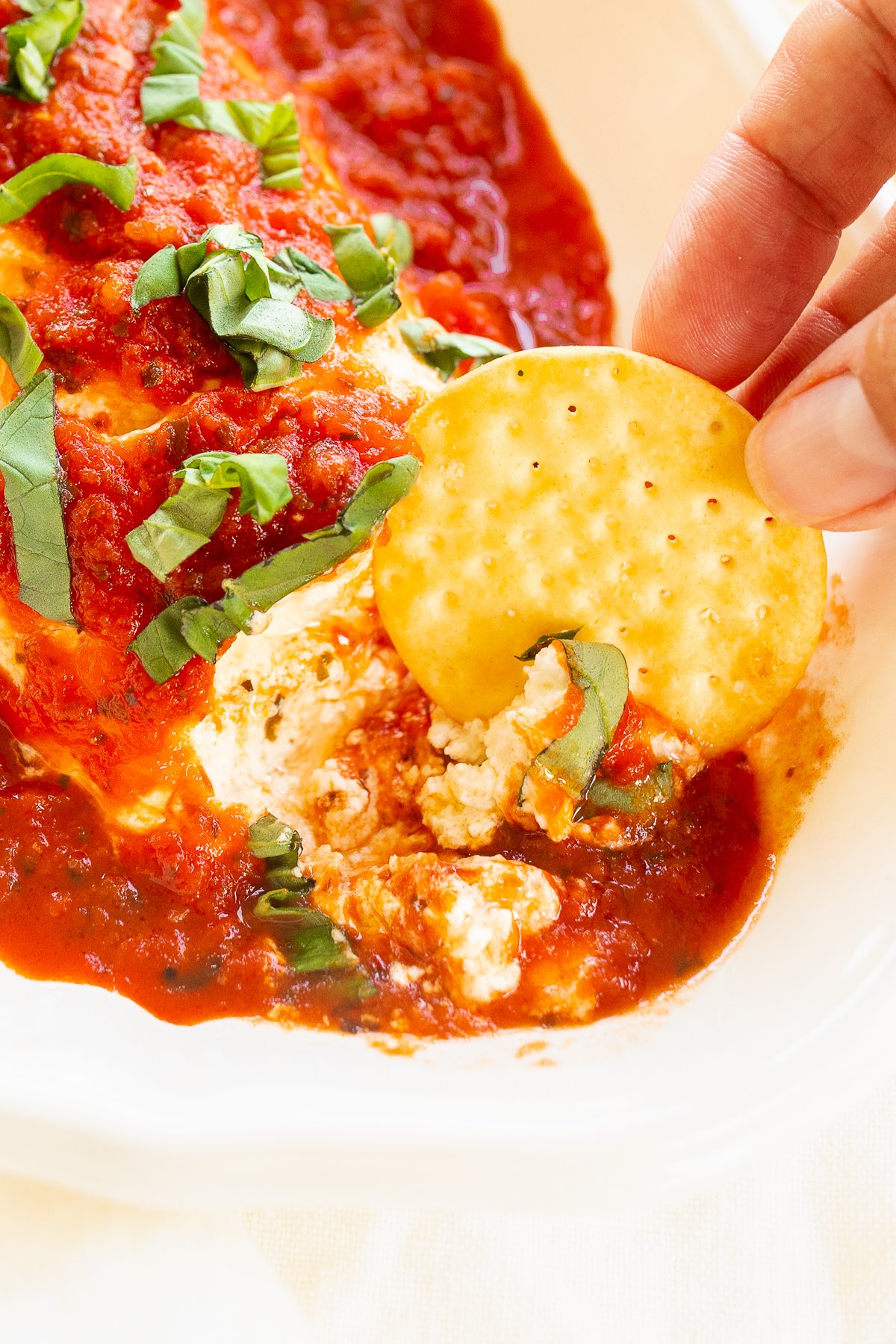 A person is dipping a cracker into a plate of queso de cabra con tomate.