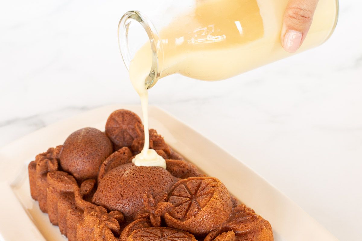 A glass jar of orange glaze pouring over an orange pound cake