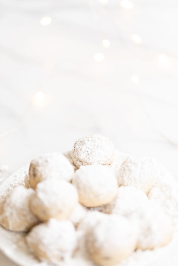 A white plate of pecan snowball cookies covered in powdered sugar.