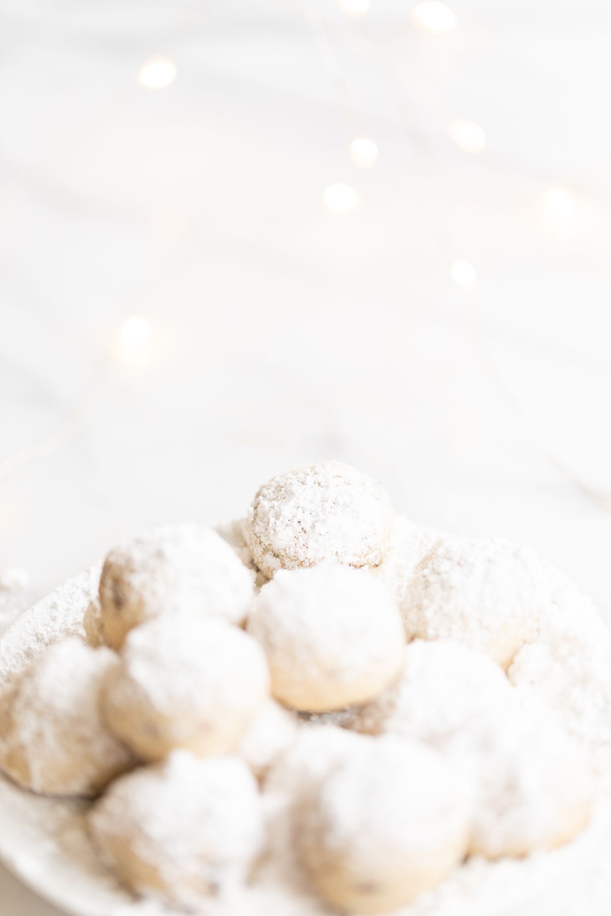 A white plate of pecan snowball cookies covered in powdered sugar.
