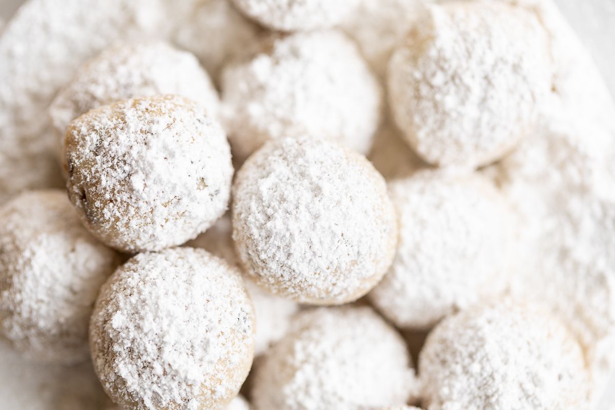 A white plate of chocolate chip pecan snowball cookies covered in powdered sugar.
