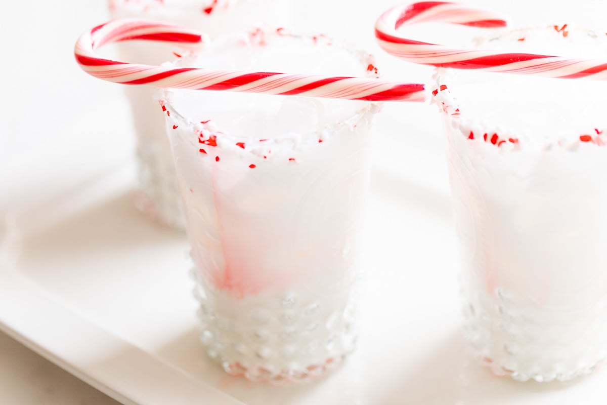 Three glasses with peppermint candy canes on a white plate.