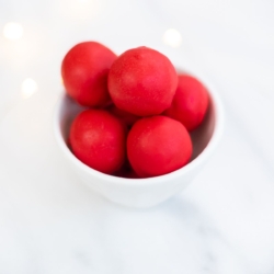 A white bowl full of red no bake Rudolph noses on a marble countertop.