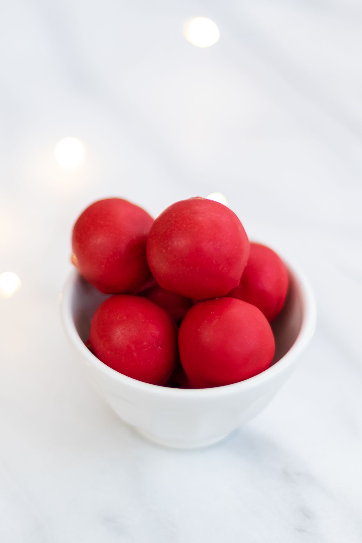 A white bowl full of red no bake Rudolph noses on a marble countertop.