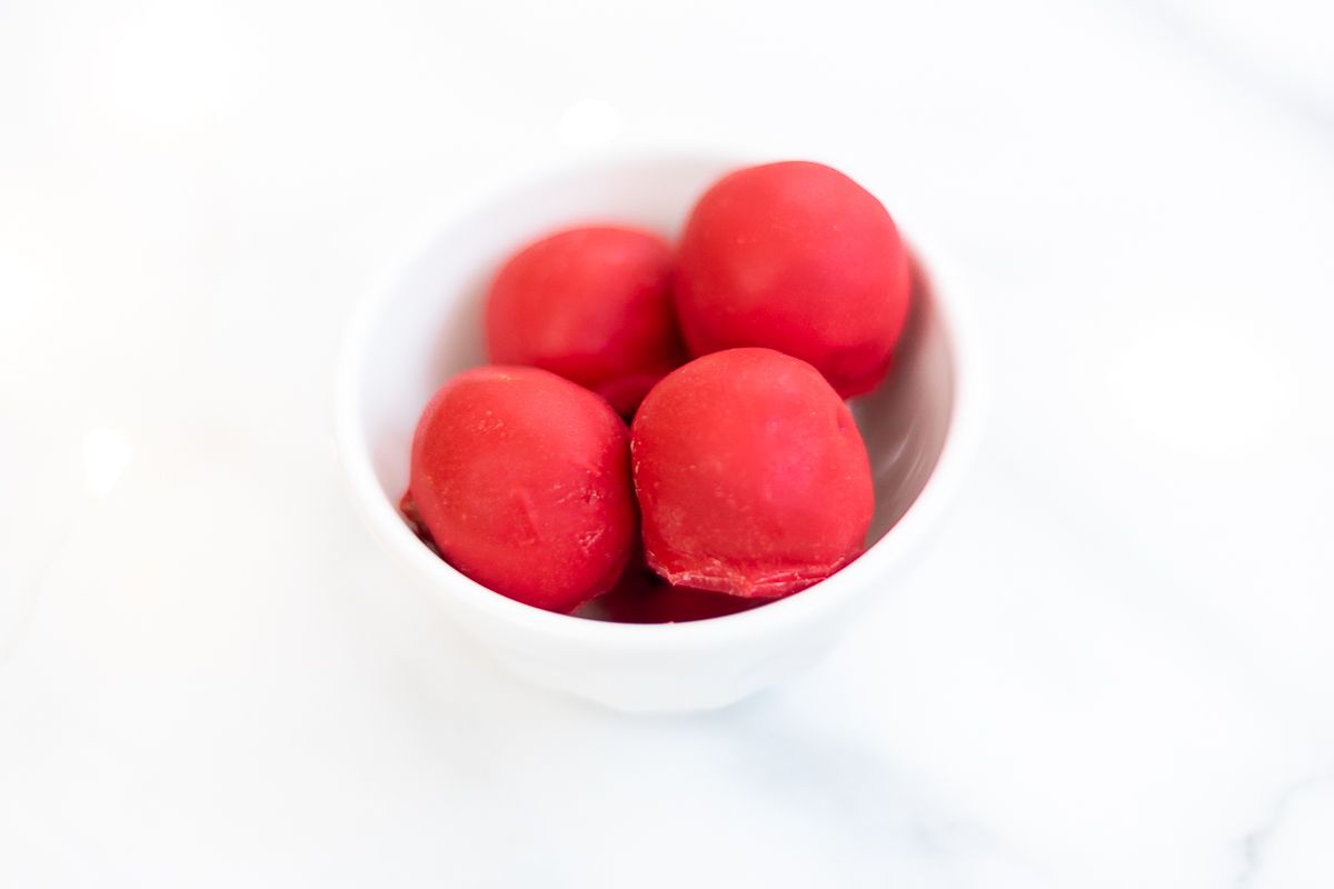 A white bowl full of red no bake Rudolph noses on a marble countertop.