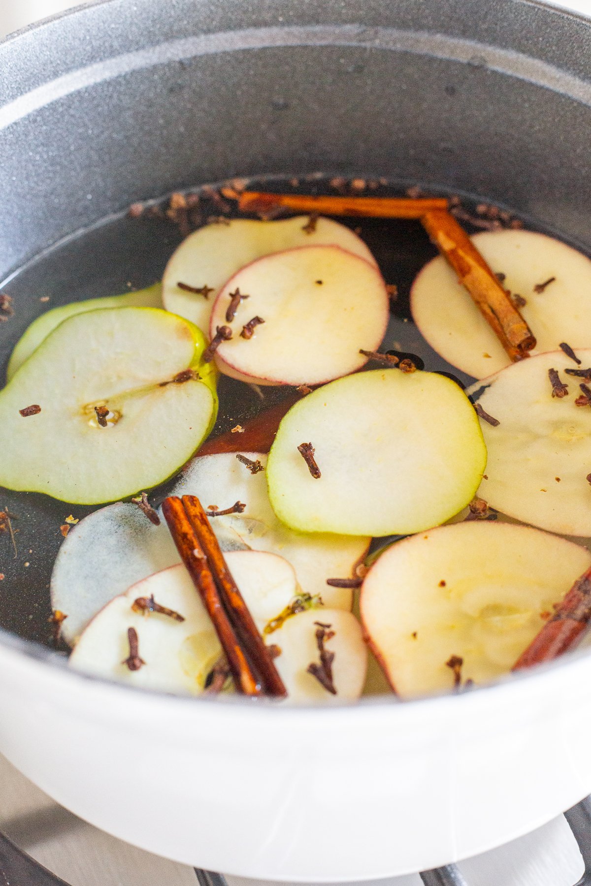 A cast iron simmer pot filled with stovetop potpourri of sliced apples, cinnamon sticks and more!