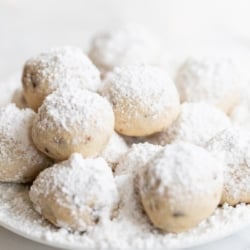 A white plate of pecan snowball cookies covered in powdered sugar.