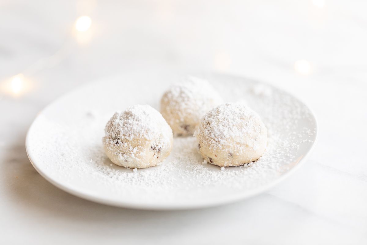 A white plate of pecan snowball cookies covered in powdered sugar.