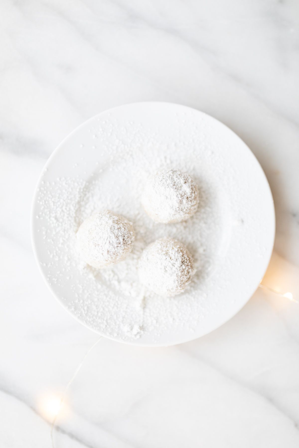 A white plate of pecan snowball cookies covered in powdered sugar.