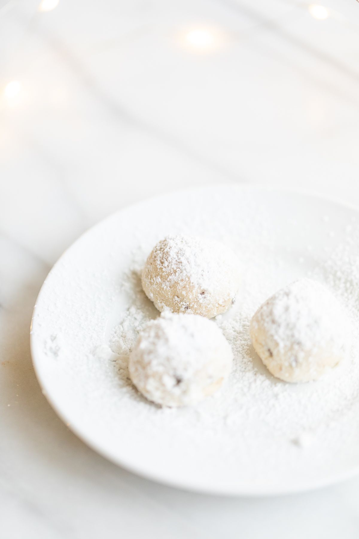 A white plate of pecan snowball cookies covered in powdered sugar.