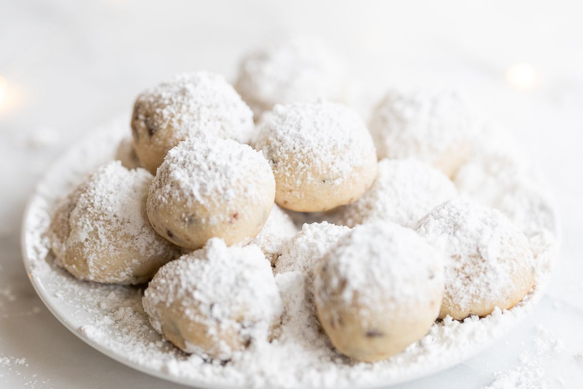 A white plate of pecan snowball cookies covered in powdered sugar.