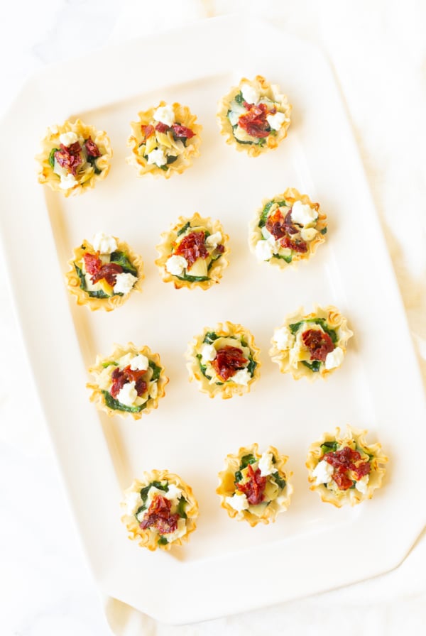 A white plate with phyllo cup appetizers and spinach dip bites on it.