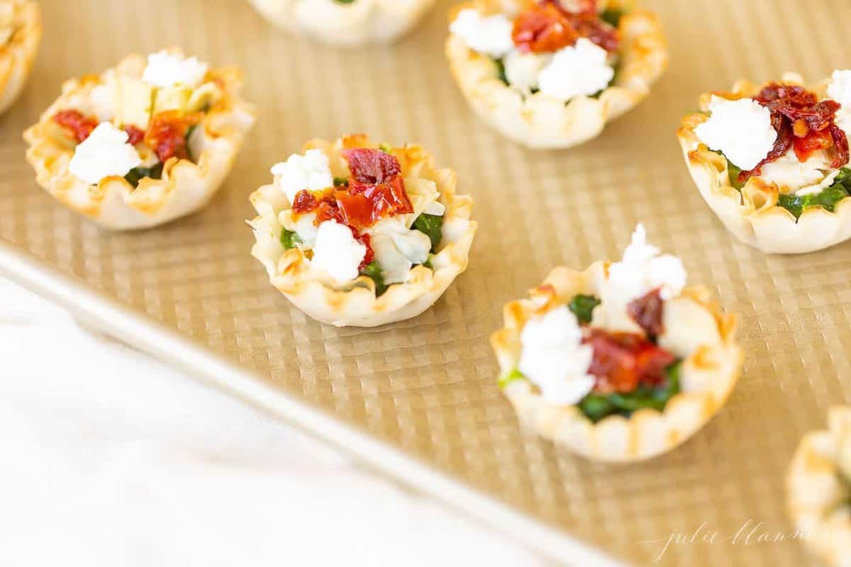 A gold baking sheet with rows of phyllo cup appetizers.